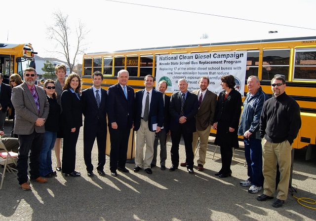State and school district officials line up for a photo in front of some brand new school buses.
