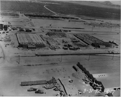 1942-03-31 Aerial view of several buildings under construction at the BMI plant. The image shows a portion of the chlorine plant including brine preparation tanks and footings (upper left) steel framing of the cell renewal building (center) chlorine cell buildings (center right and left) and drying, cooling, and liquefaction units between the cell buildings. The temporary brick grinding building is in the lower right.