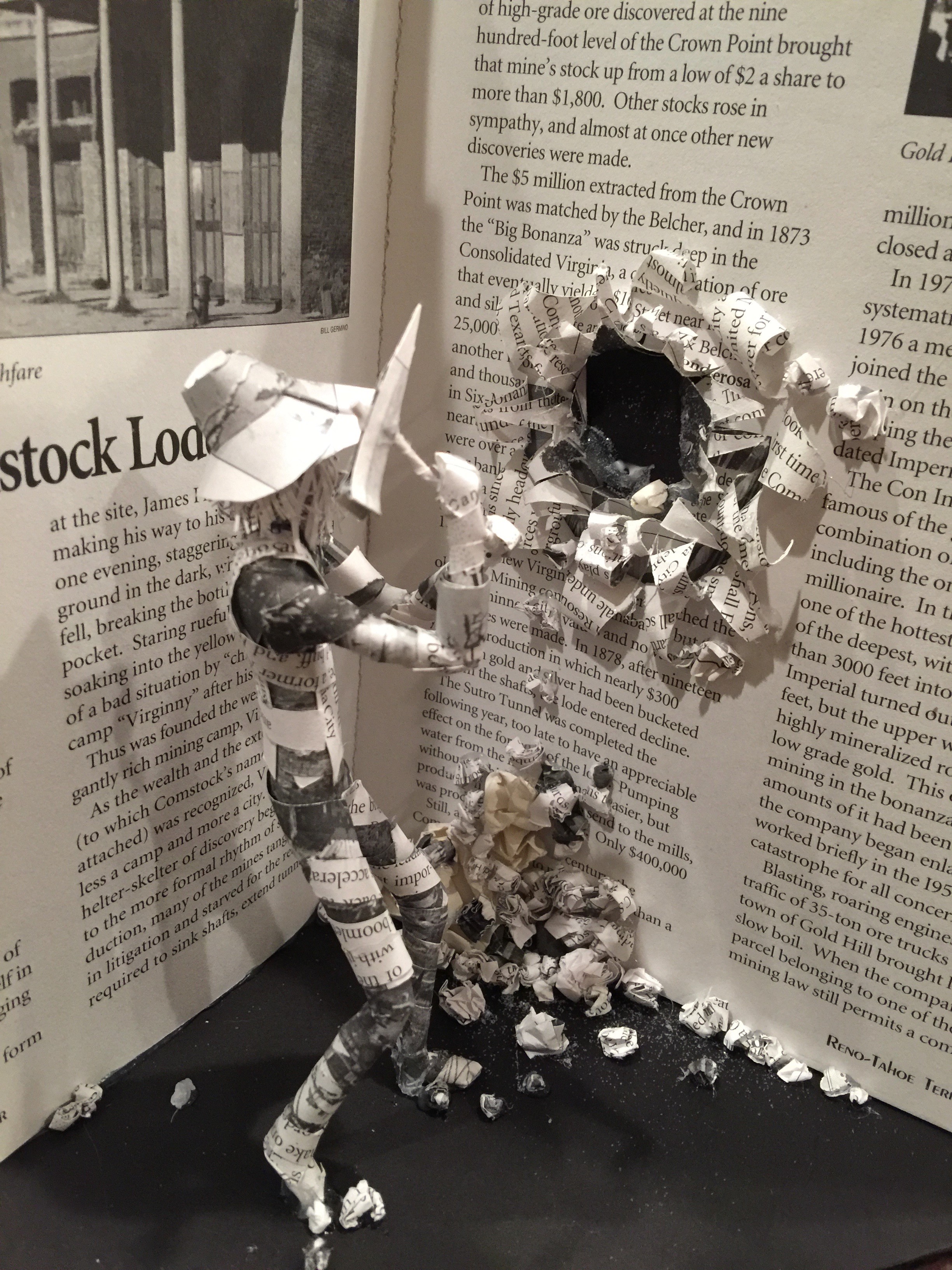 A paper sculpture of a miner digging into the depths of a book